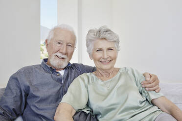 Portrait of smiling senior couple sitting on a couch in a villa - RORF02271