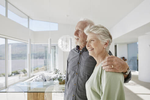 Happy senior couple in luxury beach house looking out of window - RORF02292