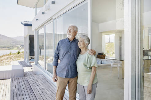 Happy senior couple standing at luxury beach house - RORF02300
