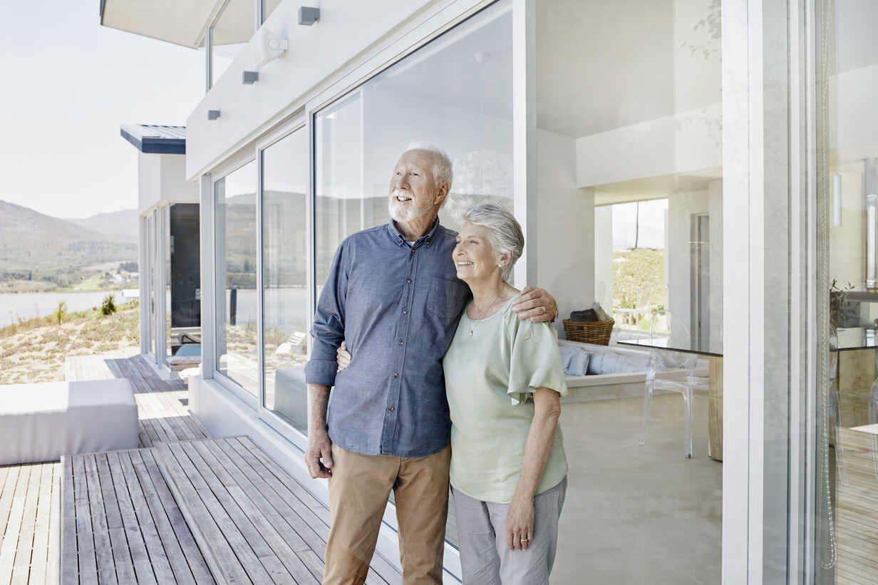 Happy senior couple standing at luxury beach house stock photo