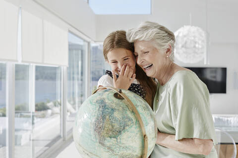 Lachende Großmutter und Enkelin mit Globus in einer Villa, lizenzfreies Stockfoto