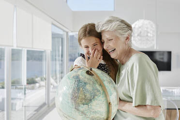 Laughing grandmother and granddaughter with globe in a villa - RORF02305