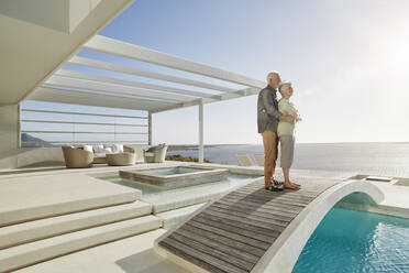 Zärtliches älteres Paar, das auf einer Brücke über einem Swimmingpool in einem luxuriösen Strandhaus steht - RORF02308