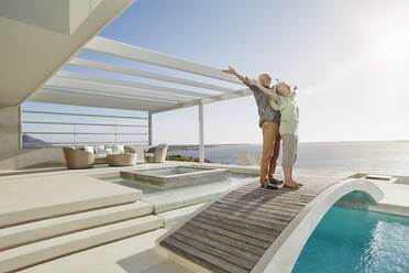 Unbeschwertes älteres Paar, das auf einer Brücke über einem Swimmingpool in einem luxuriösen Strandhaus steht - RORF02309
