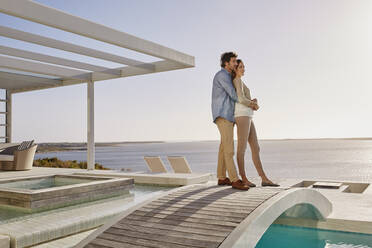 Affectionate couple standing on bridge above a swimming pool enjoying the view - RORF02313