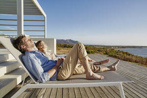 Couple lying on deck chairs at luxury beach house - RORF02324