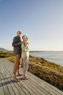 Senior couple enjoxing the view on wooden terrace at the sea - RORF02327