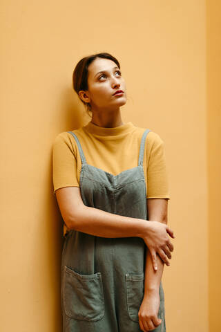 Young woman wearing jumpsuit leaning on orange wall and looking up stock photo