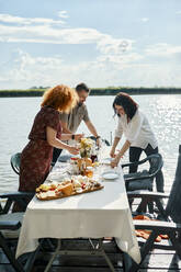 Freunde beim Abendessen an einem See, die den Tisch decken - ZEDF03515