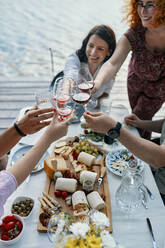 Freunde beim Abendessen am See stoßen mit Weingläsern an - ZEDF03543