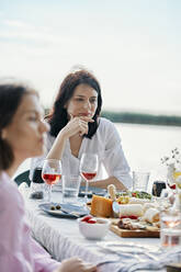 Junge Frau beim Abendessen mit Freunden am Seeufer - ZEDF03548