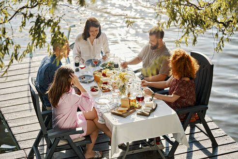 Friends having dinner on jetty at a lake - ZEDF03553