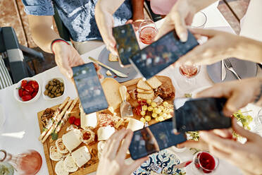 Freunde beim Abendessen mit einer Käseplatte, die mit dem Smartphone fotografieren - ZEDF03559