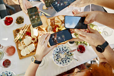 Freunde beim Abendessen mit einer Käseplatte, die mit dem Smartphone fotografieren - ZEDF03560