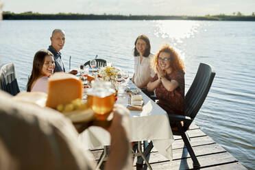 Freunde beim Abendessen an einem See mit einem Mann, der eine Käseplatte serviert - ZEDF03570