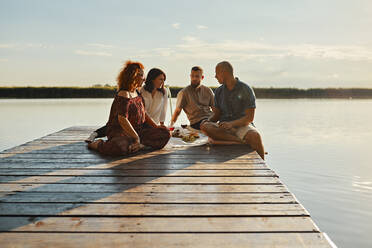 Freunde beim Picknick auf einem Steg an einem See bei Sonnenuntergang - ZEDF03579