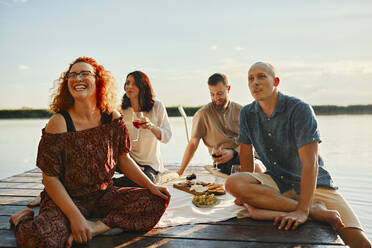 Glückliche Freunde beim Picknick auf einem Steg an einem See bei Sonnenuntergang - ZEDF03580