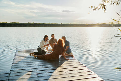 Freunde beim Picknick auf einem Steg an einem See bei Sonnenuntergang, lizenzfreies Stockfoto