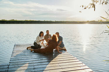 Freunde beim Picknick auf einem Steg an einem See bei Sonnenuntergang - ZEDF03583