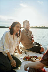 Friends having picnic on jetty at a lake at sunset - ZEDF03585