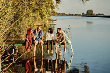 Freunde, die sich im Wasser spiegeln, sitzen auf einem Steg an einem See - ZEDF03596
