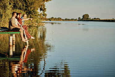 Freunde, die sich im Wasser spiegeln, sitzen auf einem Steg an einem See - ZEDF03597