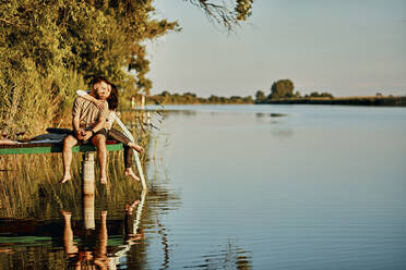 Affectionate couple reflected in water sitting on jetty at a lake - ZEDF03600
