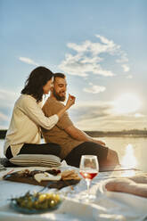 Couple having picnic on jetty at a lake at sunset - ZEDF03602