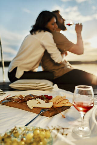 Paar beim Picknick auf einem Steg an einem See bei Sonnenuntergang, lizenzfreies Stockfoto