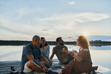 Freunde beim Picknick auf einem Steg an einem See bei Sonnenuntergang - ZEDF03617