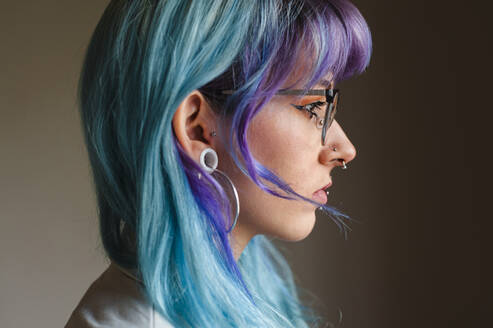 Nahaufnahme einer nachdenklichen jungen Frau mit gefärbtem Haar und Piercings an der Wand in einem alten Büro - JMPF00126