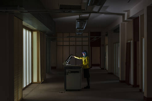 Businesswoman with dyed hair operating photocopier standing in old abandoned office - JMPF00127