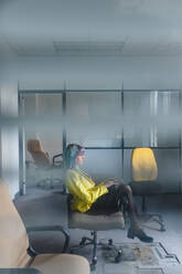 Thoughtful businesswoman sitting on chair in old office seen through window - JMPF00133