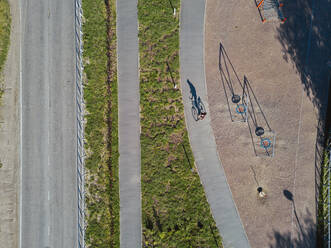 Russia, Tikhvin, Man riding bicycle on path near park playground, aerial view - KNTF04848