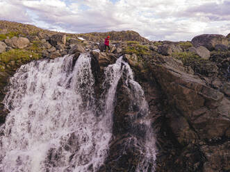 Russland, Gebiet Murmansk, Teriberka, Luftaufnahme einer Wanderin am Rande eines plätschernden Wasserfalls - KNTF04897