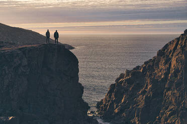 Silhouette men standing on cliff during sunset at Teriberka, Murmansk Oblast, Russia - KNTF04903