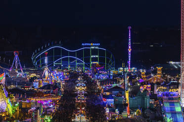 Deutschland, Bayern, München, Drohnenaufnahme von Menschenmassen, die das Oktoberfest in einem großen beleuchteten Vergnügungspark bei Nacht feiern - MMAF01356