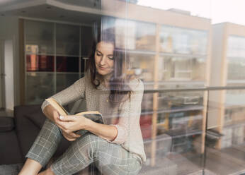 Lovely adult lady in elegant outfit smiling and looking away while lying on comfortable sofa with interesting book - ADSF00158