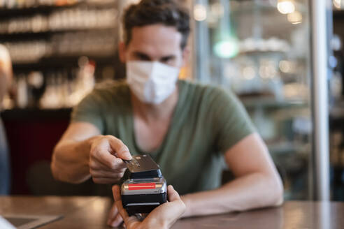 Man with protective mask paying with credit card in restaurant - DIGF12747
