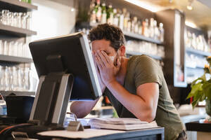 Restaurant manager with hands in face during corona crisis - DIGF12754