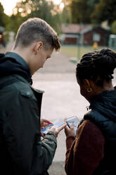 Männliche und weibliche Freunde im Teenageralter nutzen eine Smartphone-App, während sie auf der Straße stehen - MASF18643