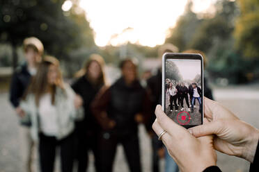 Cropped hands of woman with smart phone filming teenagers dancing on street in city - MASF18647