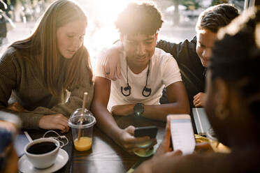 Teenage girls and boys surfing internet on mobile phones while sitting in cafe - MASF18652