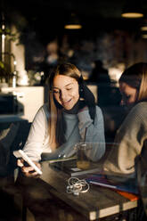 Lächelndes Teenager-Mädchen, das einem Freund sein Smartphone zeigt, während es in einem Cafe sitzt - MASF18653