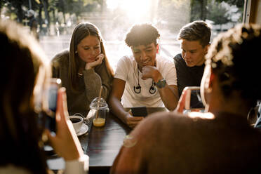 Mädchen und Jungen im Teenageralter nutzen soziale Medien auf Smartphones, während sie in einem Café sitzen - MASF18654