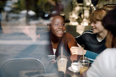 Lächelndes Teenager-Mädchen mit Freunden im Café durch ein Glasfenster gesehen - MASF18655
