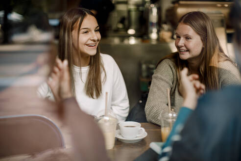 Lächelnde Teenager-Mädchen im Gespräch mit Freunden, während sie in einem Café sitzen - MASF18657