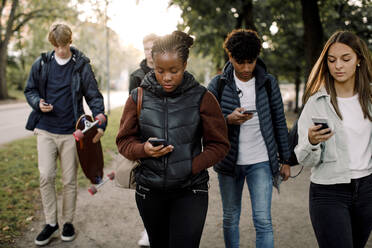 Multiethnische Teenager-Freunde benutzen Smartphones, während sie in der Stadt auf der Straße gehen - MASF18660