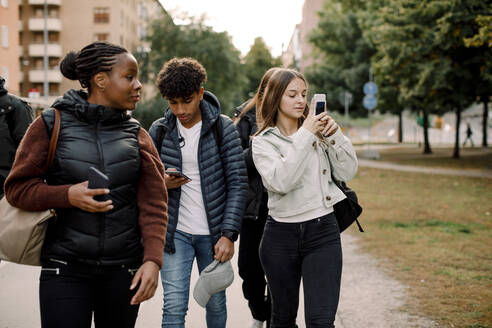 Teenager-Mädchen und Junge mit Handy beim Gehen auf der Straße in der Stadt - MASF18663