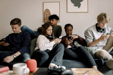 Multi-ethnic friends using social media on mobile phones while sitting on sofa at home - MASF18667